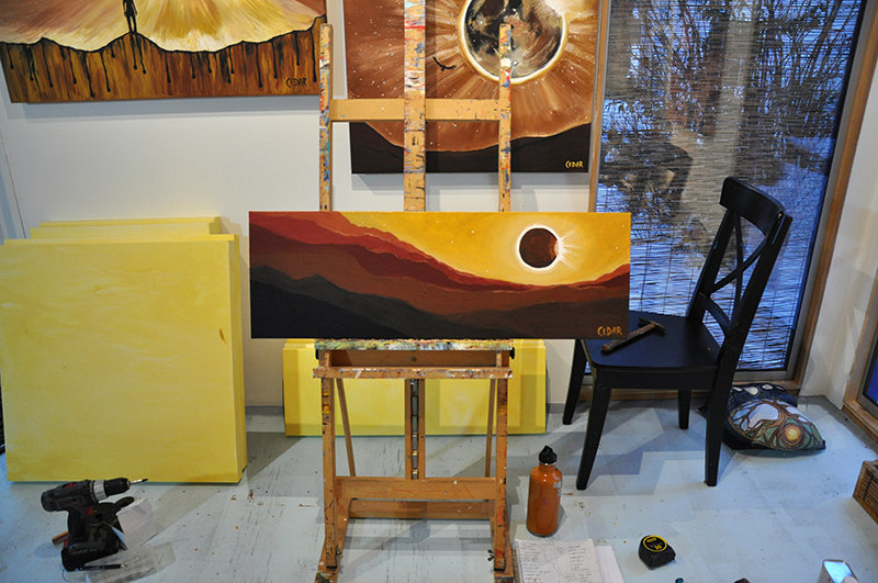 Paintings in art studio of Cedar Lee. On easel: Eclipse Over Red Hills. 12" x 36", Oil on Canvas, © 2017 Cedar Lee